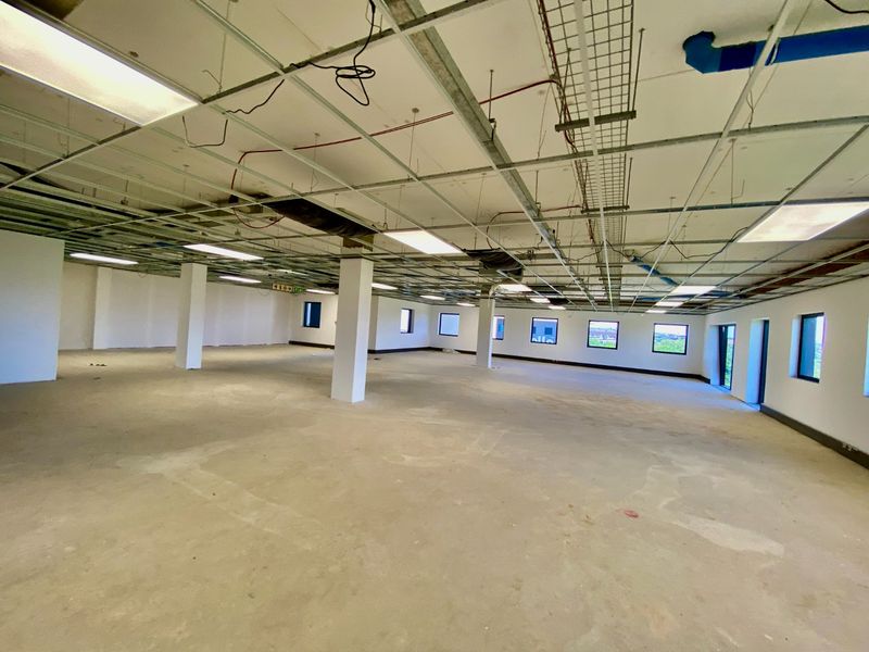 Large open-plan commercial office space in shell condition, featuring exposed ceiling grid, structural columns, and concrete flooring, ready for custom fit-out.