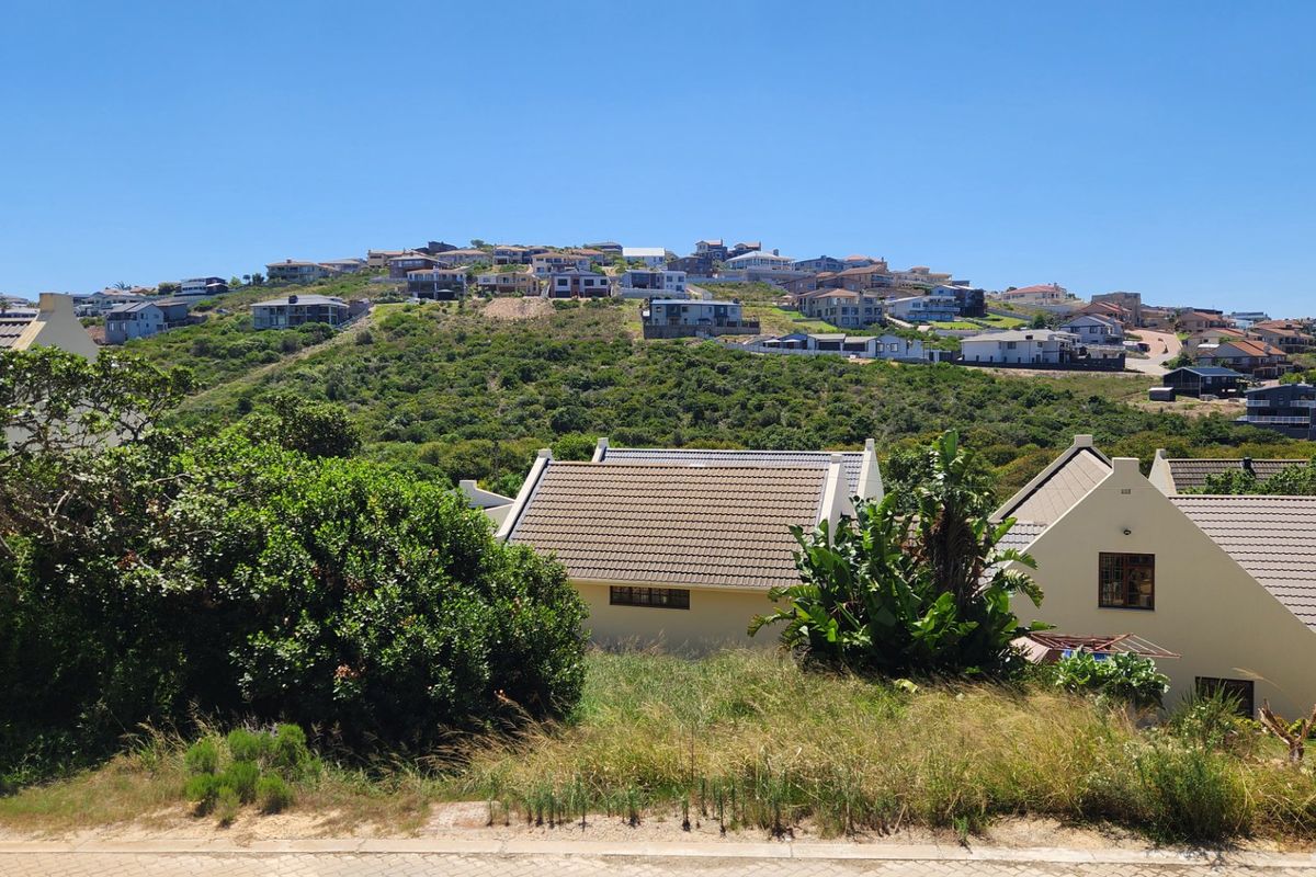 A scenic view overlooking a residential hillside development with established homes and natural coastal vegetation under a clear blue sky.
