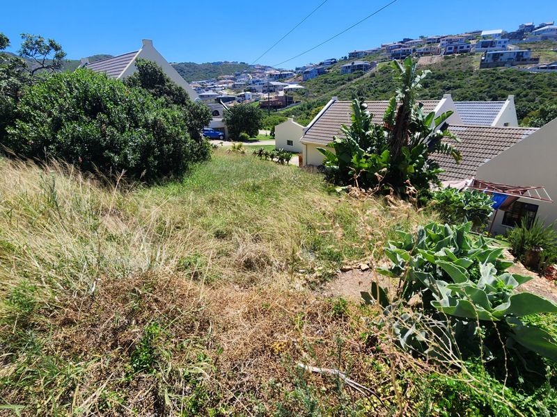 A vacant residential plot featuring sloped terrain, situated within an established neighborhood with surrounding residential properties.