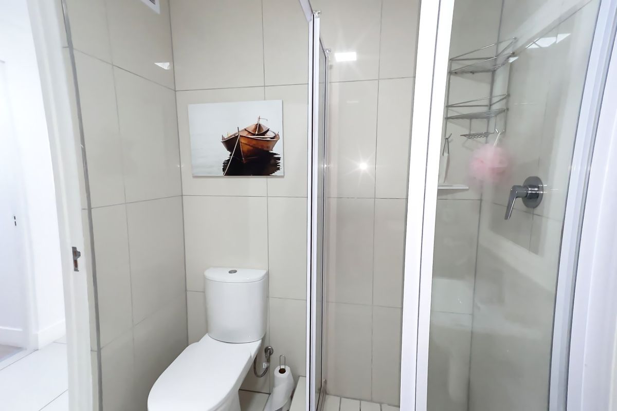 A clean, modern bathroom featuring a glass-enclosed shower and a standard toilet with neutral wall tiling.