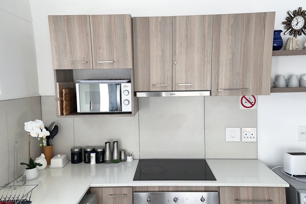 Modern kitchen featuring wood-grain cabinetry, stone countertops, an integrated electric hob, oven, and extractor fan with convenient floating shelving.
