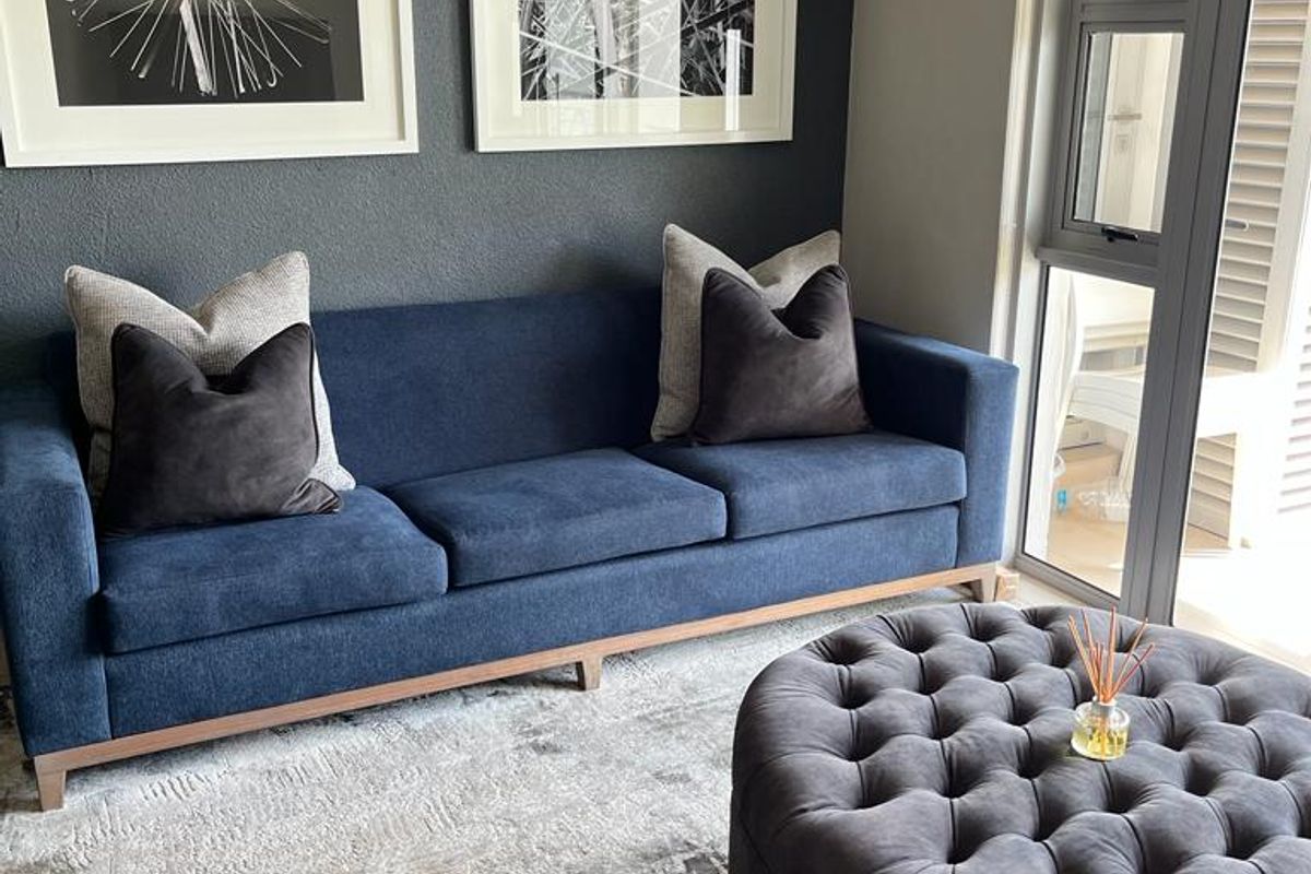 A modern living room featuring a dark accent wall, neutral flooring, and large aluminium-framed windows with roller blinds.