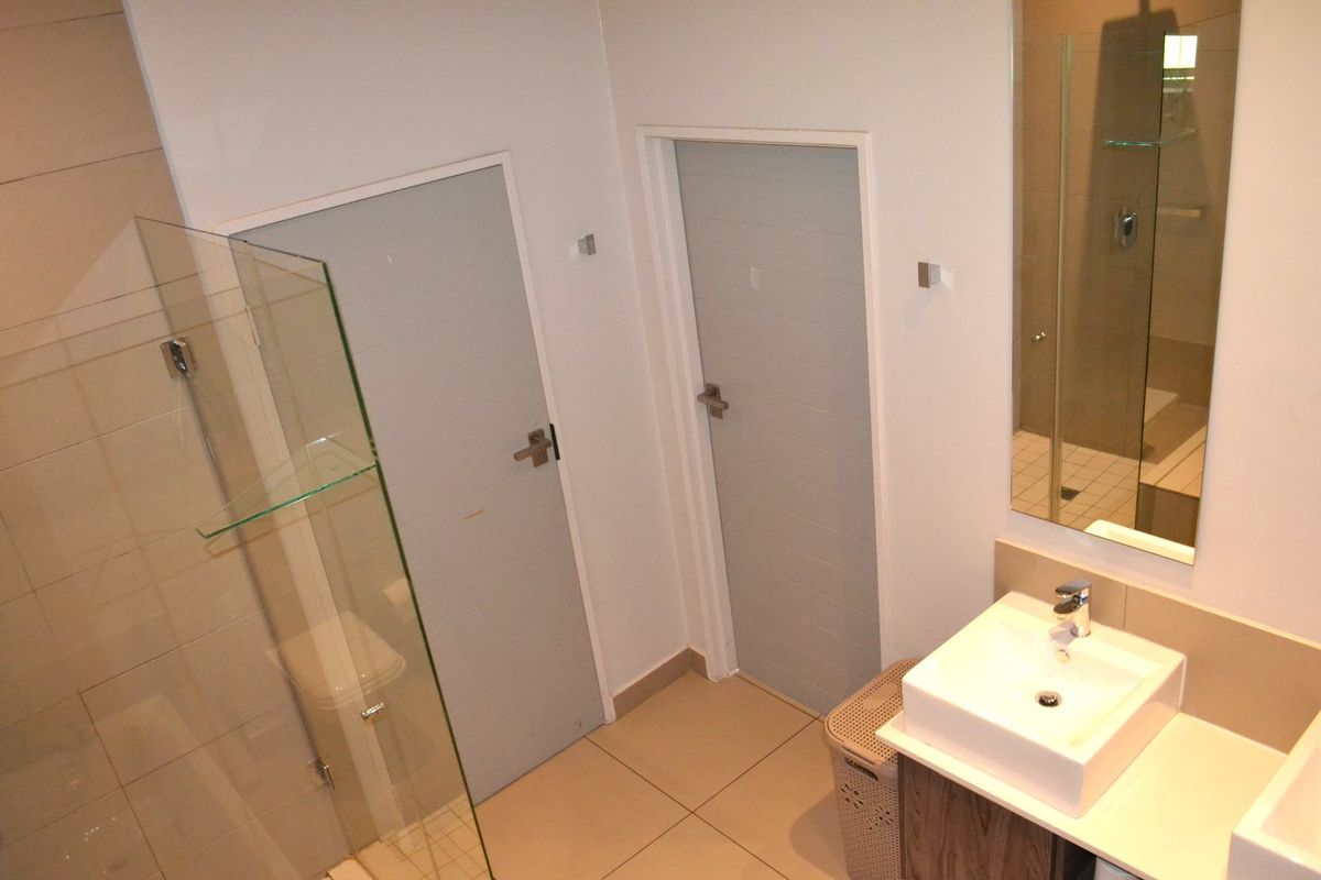Modern bathroom featuring a glass shower enclosure, vanity basin with mixer tap, and neutral wall and floor tiling.