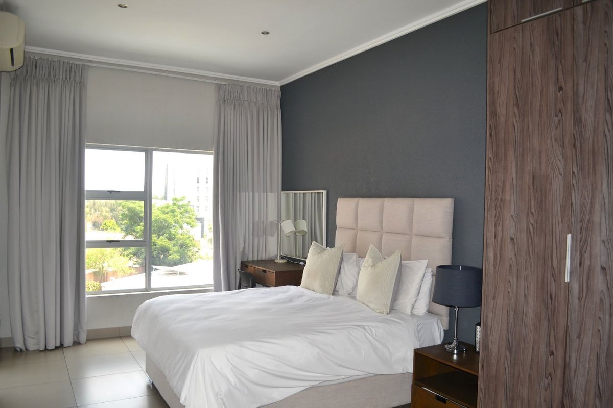 A well-maintained bedroom featuring tiled flooring, built-in cupboards, an air conditioning unit, and large windows allowing for natural light.