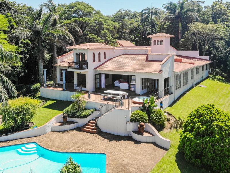 Aerial view of a Mediterranean-style residence featuring a tiled roof, expansive rear patio, swimming pool, and landscaped garden surroundings.