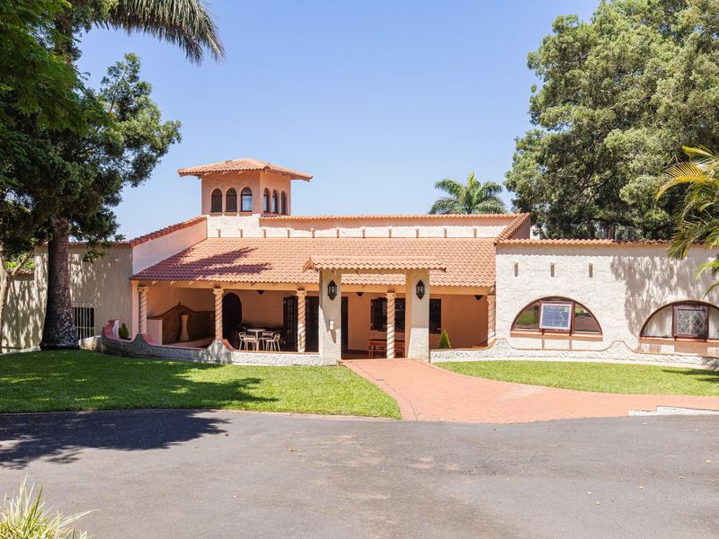 Front elevation of a Mediterranean-style house featuring a covered patio, terracotta roof tiles, a central tower, and arched windows set in a landscaped garden.
