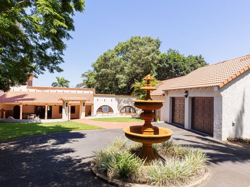 Spacious front courtyard featuring a paved driveway, double garage, covered entrance, and a central decorative fountain set within a landscaped garden.