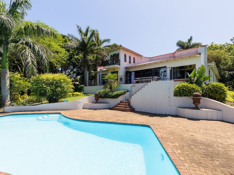 A spacious rear exterior view featuring a swimming pool, paved patio area, and a multi-level house with a balcony and landscaped garden.