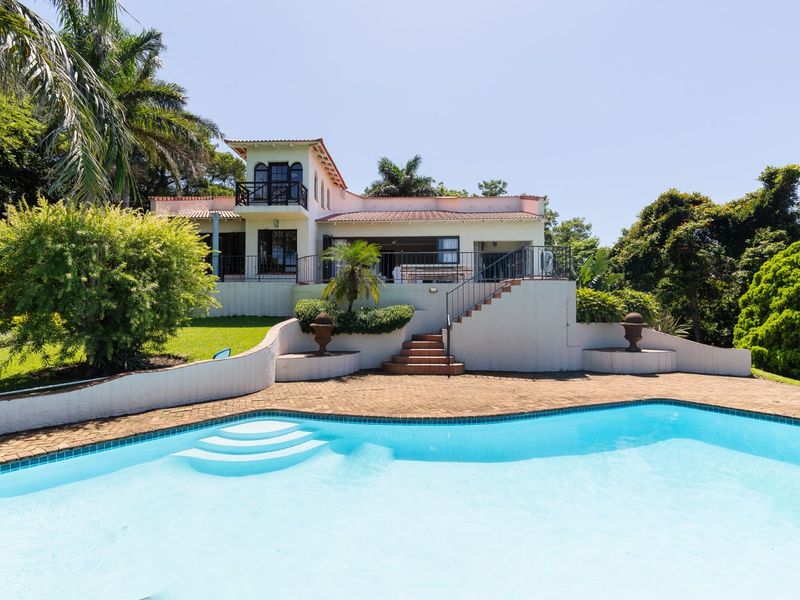 A spacious rear exterior view featuring a swimming pool, paved patio area, and a multi-level house with a balcony and landscaped garden.