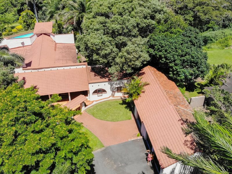 Aerial view of a spacious residential property featuring a terracotta tiled roof, paved driveway, central courtyard, and lush surrounding garden landscape.