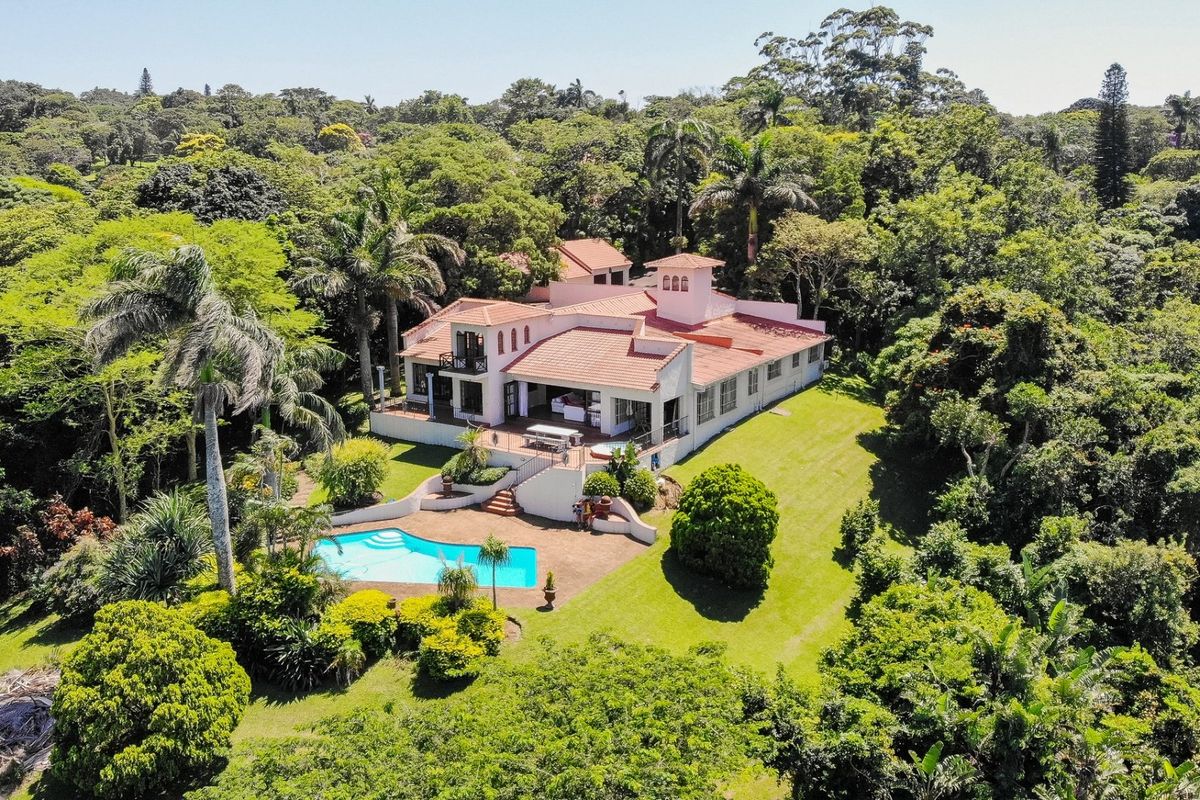 Aerial view of a large residential property featuring a tiled roof, expansive garden, and a private swimming pool set within a lush, wooded landscape.