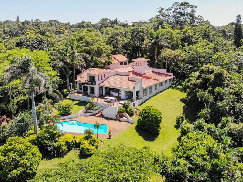 Aerial view of a large residential property featuring a tiled roof, expansive garden, and a private swimming pool set within a lush, wooded landscape.