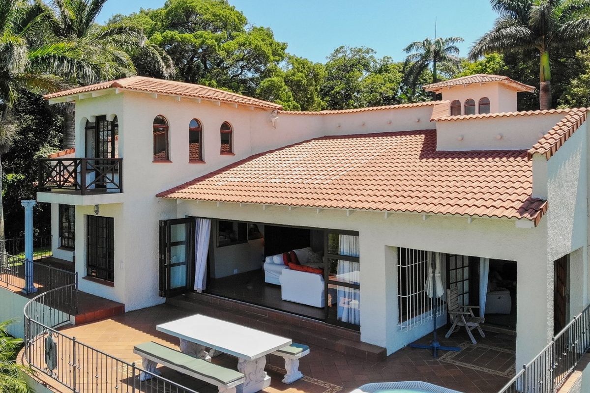 Aerial view of a Mediterranean-style home featuring a terracotta tiled roof, a spacious covered patio, and an open-plan living area with large folding doors.