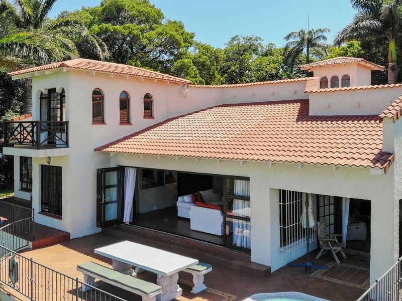 Aerial view of a Mediterranean-style home featuring a terracotta tiled roof, a spacious covered patio, and an open-plan living area with large folding doors.
