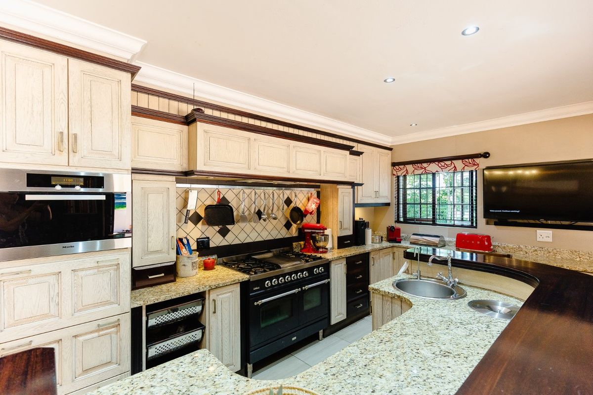 A traditional kitchen featuring granite countertops, a built-in Miele oven, a large gas range, and extensive cabinetry with a classic wood-grain finish.