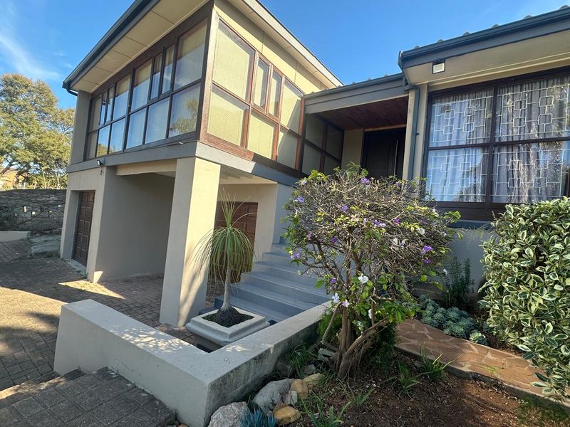 Front elevation of a multi-level residence featuring a paved driveway, concrete staircase, and large glass-paneled windows with timber framing.