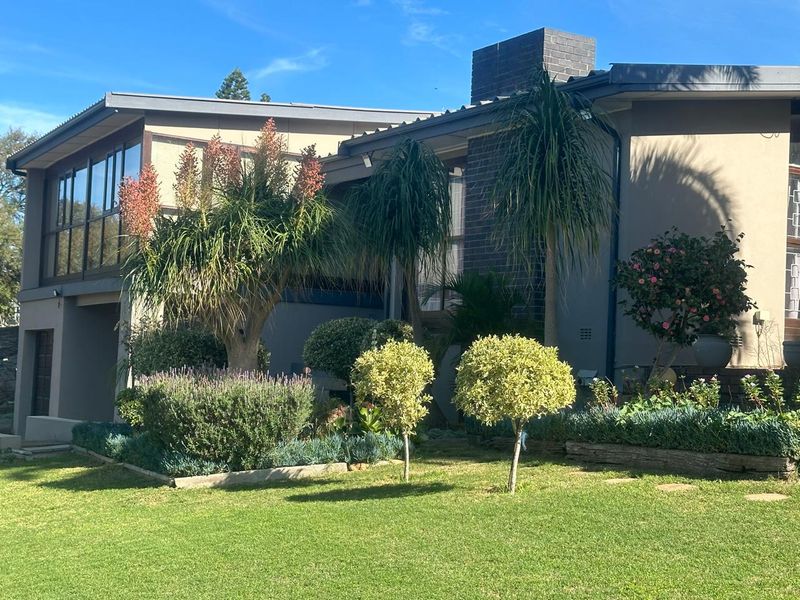 A view of the rear exterior facade featuring a brick chimney, large windows, and a well-maintained garden with established landscaping.