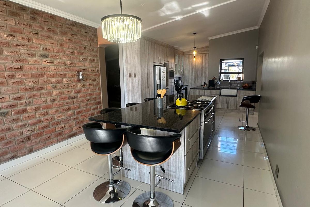 Modern kitchen featuring a large central island with granite countertops, built-in cabinetry, gas hob, and a distinctive exposed brick feature wall.