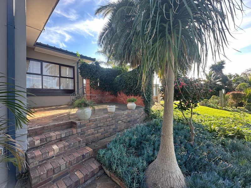 A raised brick patio area featuring stone paving, steps, and established garden landscaping, providing an outdoor space adjacent to the main house structure.