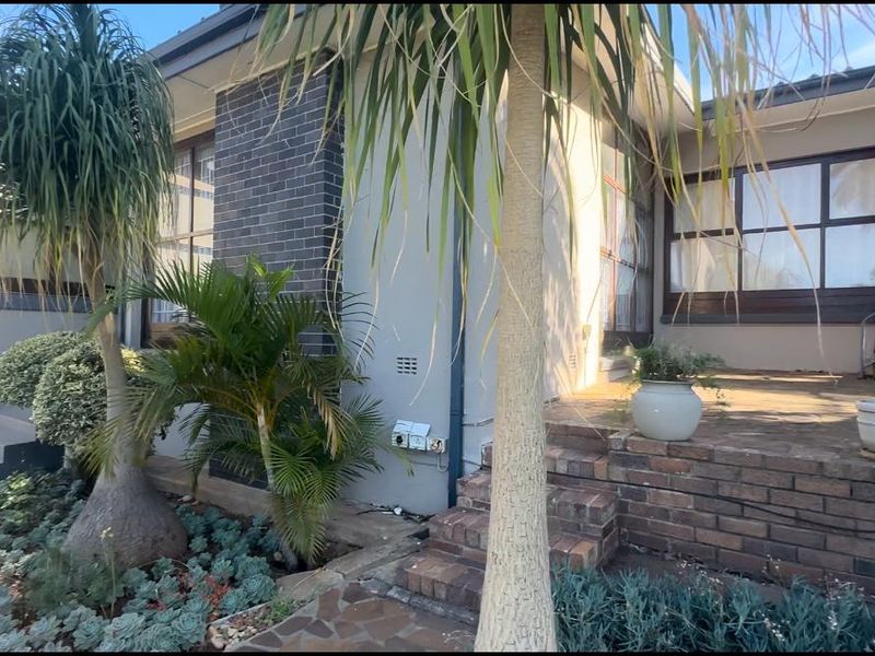 A well-maintained exterior front facade featuring brick masonry accents, a paved patio area, and established garden landscaping.