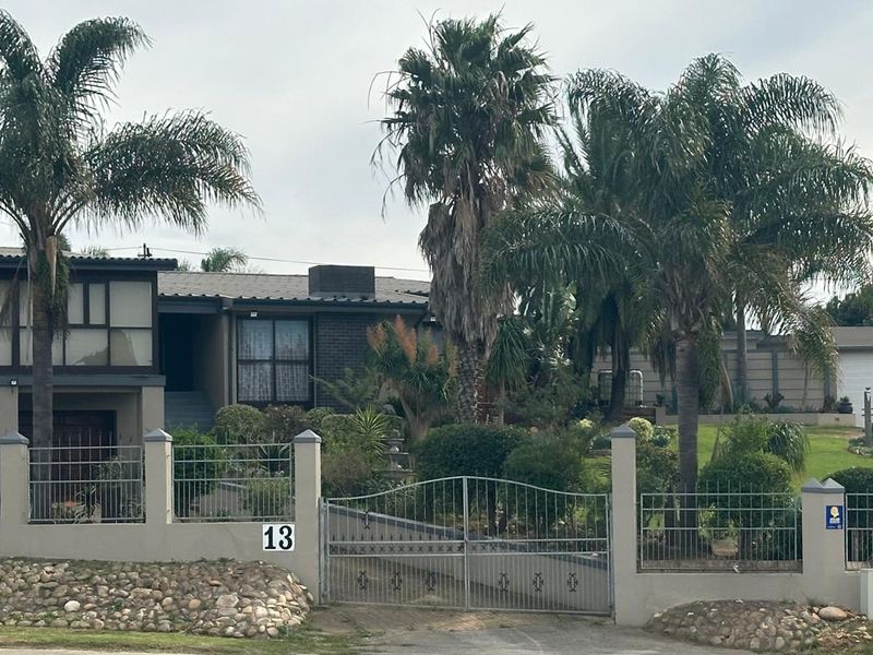 Front view of a residential property featuring a gated entrance, established garden with mature palm trees, and a multi-level facade.