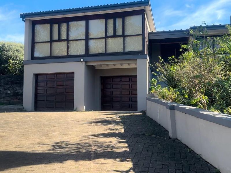 Front elevation of a double-story house featuring two wooden garage doors, a paved driveway, and a landscaped garden area.