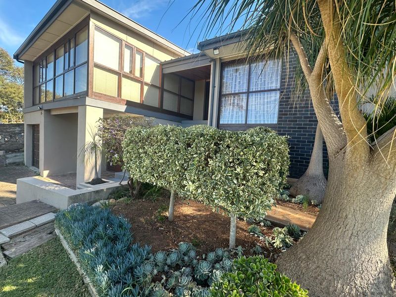Front elevation of a multi-level residence featuring a mix of brick and rendered finishes, large glass windows, and established garden landscaping.