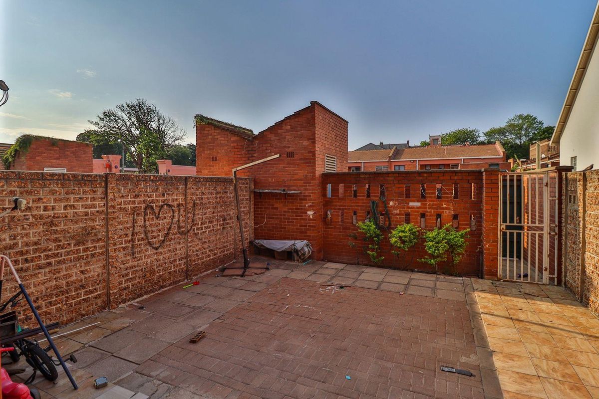 A private rear courtyard featuring brick boundary walls, paved flooring, and a secure metal gate entrance.