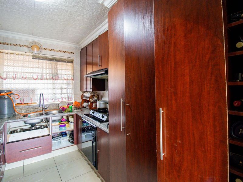 Compact kitchen featuring dark wood cabinetry, granite countertops, built-in oven, hob, extractor fan, and a dedicated wine storage rack.