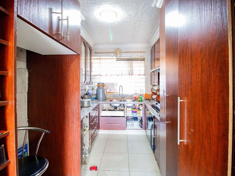 A galley-style kitchen featuring dark wood-look cabinetry, granite countertops, a double sink, and tiled flooring with a textured ceiling finish.