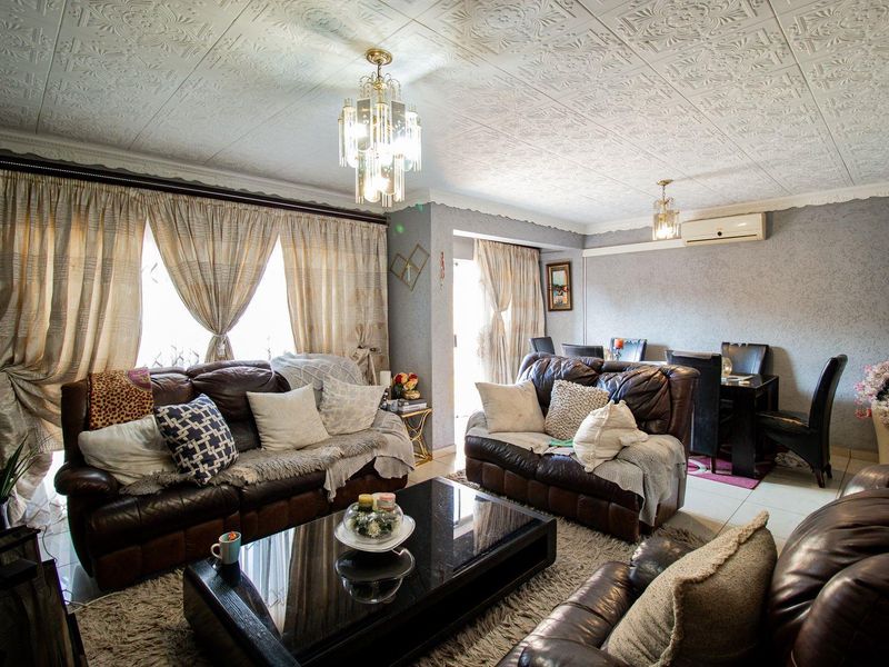 Open-plan living and dining area featuring textured ceiling tiles, crystal chandeliers, and split-system air conditioning with access to an outdoor space.
