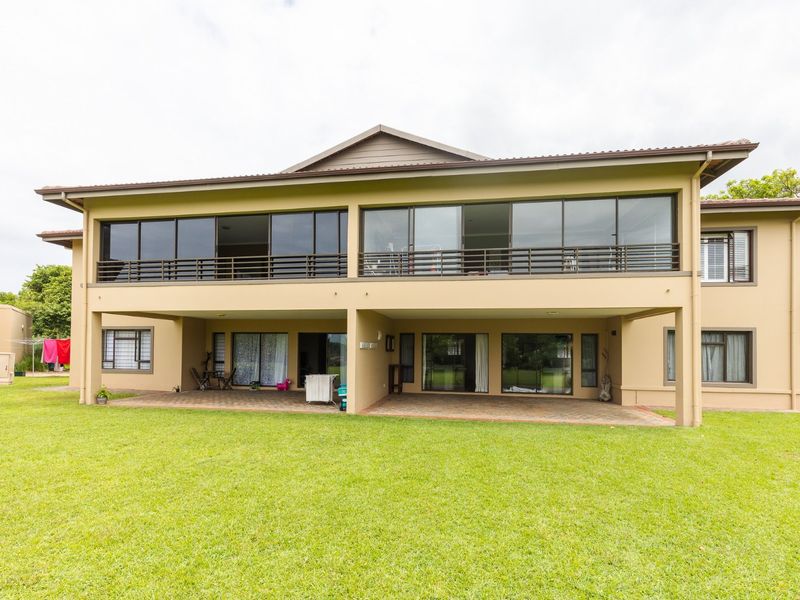 Rear view of the apartment building featuring a spacious ground floor patio, an upper-level balcony with metal railings, and large sliding glass doors.