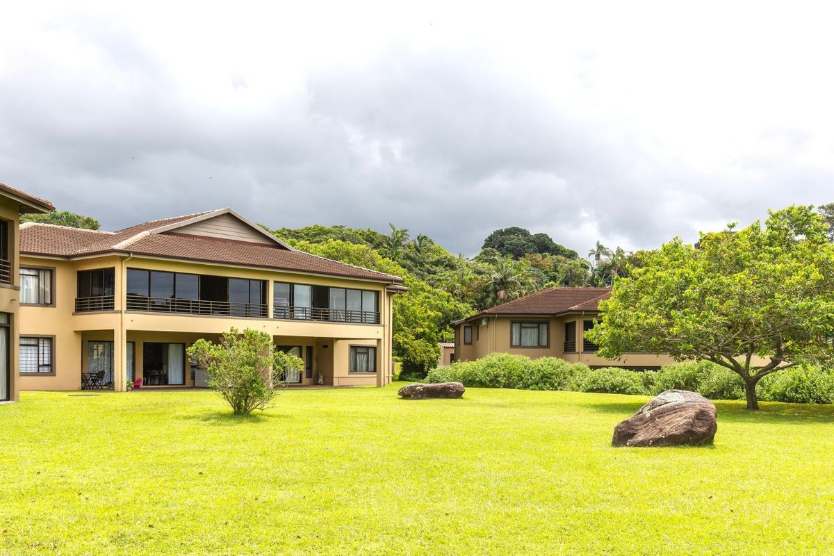 A view of the rear elevation of the apartment complex featuring a spacious lawn, balconies with metal railings, and large sliding glass doors.