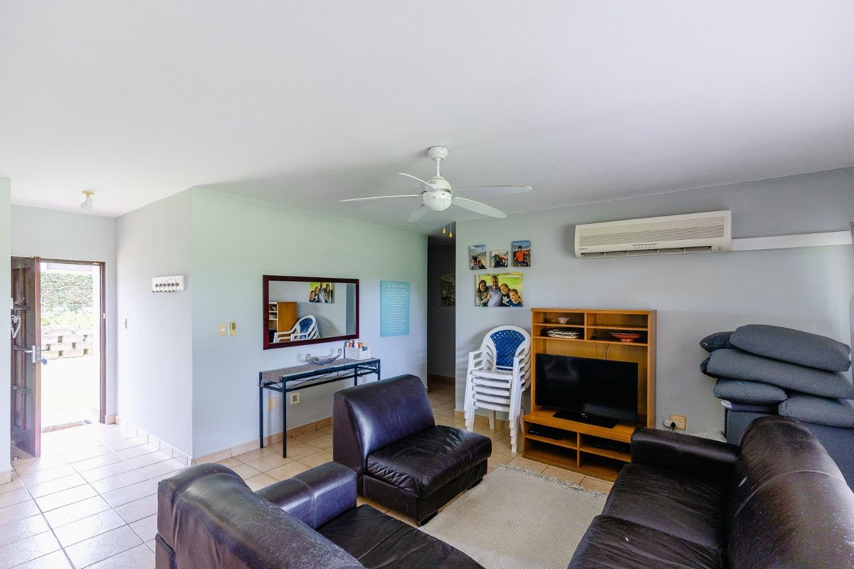 A functional living room featuring tiled flooring, a ceiling fan, and a wall-mounted air conditioning unit, with direct access to an outdoor area.