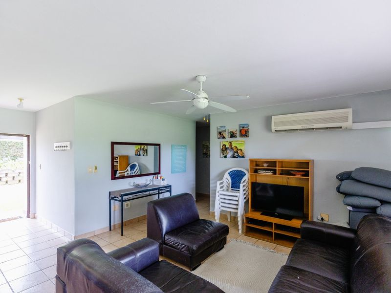 A functional living room featuring tiled flooring, a ceiling fan, and a wall-mounted air conditioning unit, with direct access to an outdoor area.