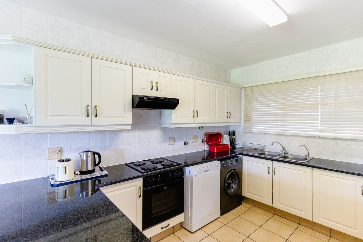 A functional kitchen featuring granite countertops, white cabinetry, tiled backsplash, and integrated electric cooking appliances with a double basin sink.