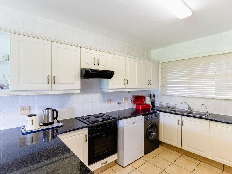 A functional kitchen featuring granite countertops, white cabinetry, tiled backsplash, and integrated electric cooking appliances with a double basin sink.