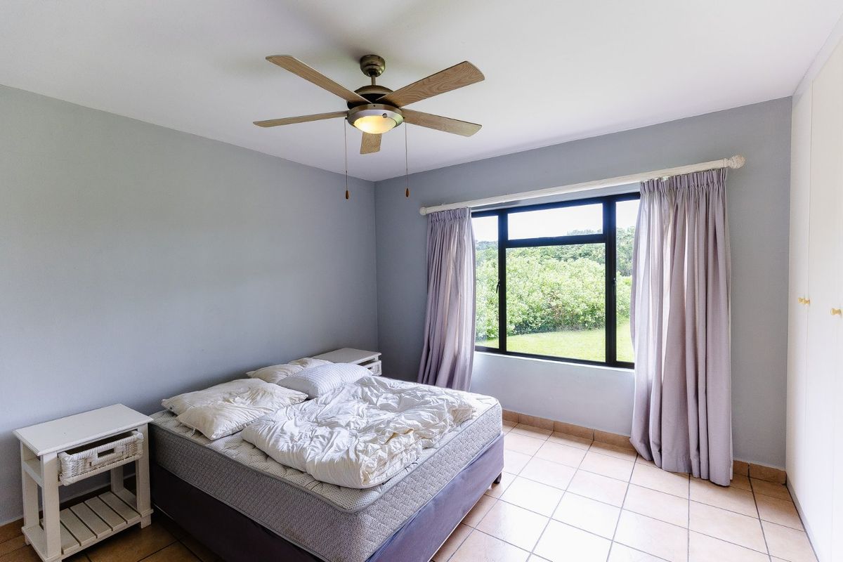 A bedroom featuring tiled flooring, a ceiling fan, and a built-in wardrobe, with a window providing natural light and garden views.