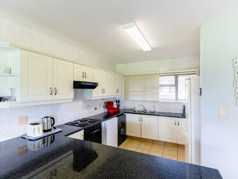 A functional kitchen featuring granite countertops, ample built-in cabinetry, an electric hob with extractor, and a double bowl sink with tiled finishes.