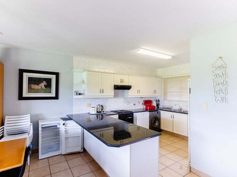 Functional kitchen featuring granite countertops, white cabinetry, built-in oven and hob, and tiled flooring with an integrated laundry area.