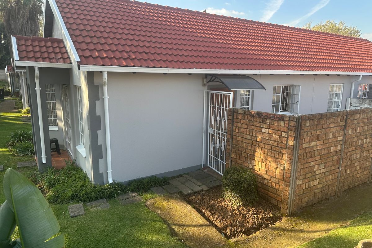 Rear exterior view of the property featuring a tiled roof, brick boundary wall, and a paved entrance area with security gate.