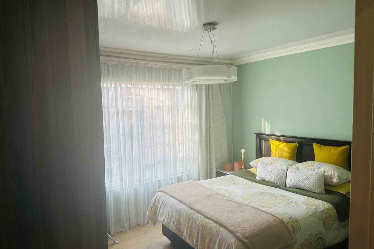 A well-lit bedroom featuring laminate flooring, crown molding, and a central pendant light fixture, offering a comfortable and functional living space.