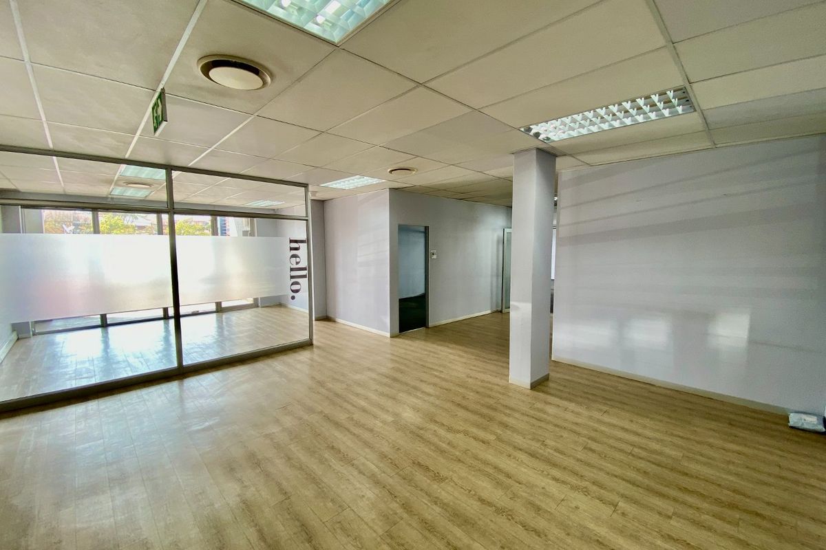 Open-plan commercial office space featuring laminate flooring, a glass partition wall, and a suspended ceiling with recessed lighting.