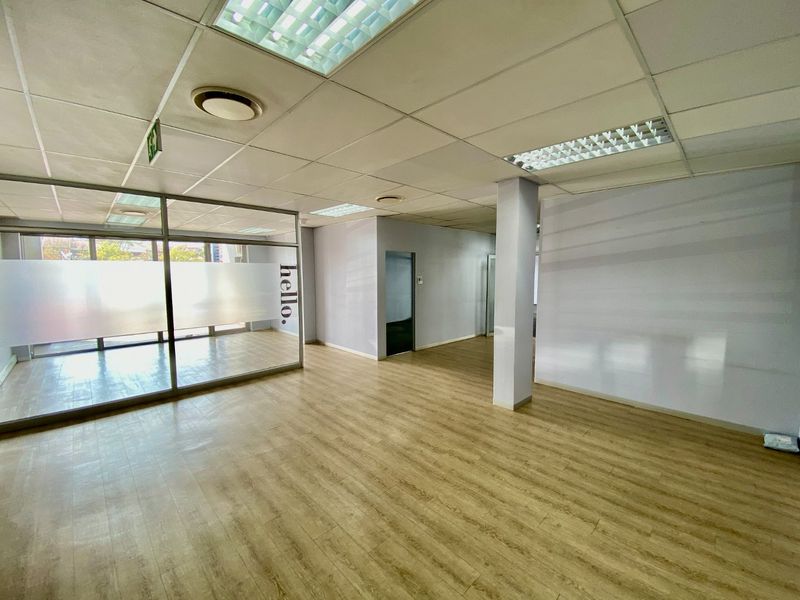 Open-plan commercial office space featuring laminate flooring, a glass partition wall, and a suspended ceiling with recessed lighting.
