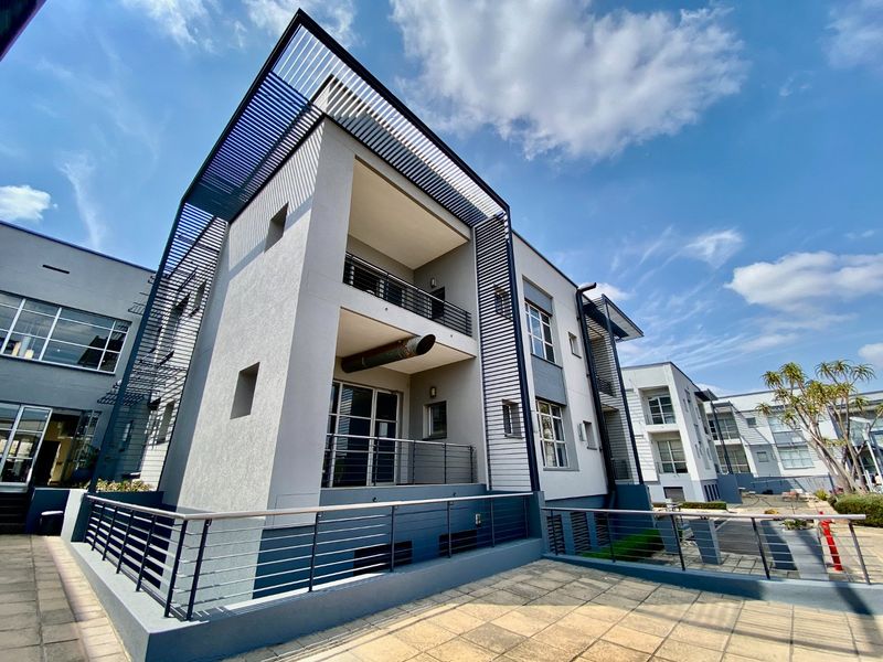 Modern commercial building exterior featuring multi-level balconies, metal architectural detailing, and a paved terrace area.