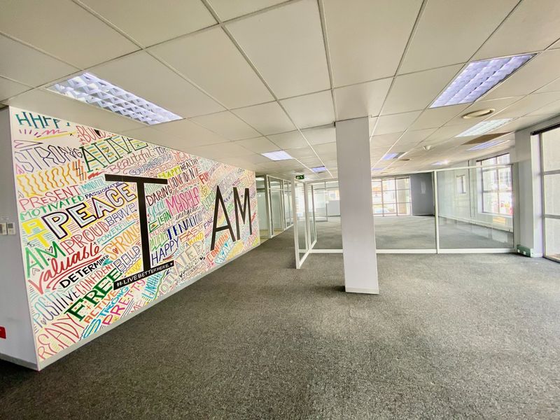 Open-plan commercial office space featuring glass partitioning, carpeted flooring, and a suspended ceiling with recessed lighting.