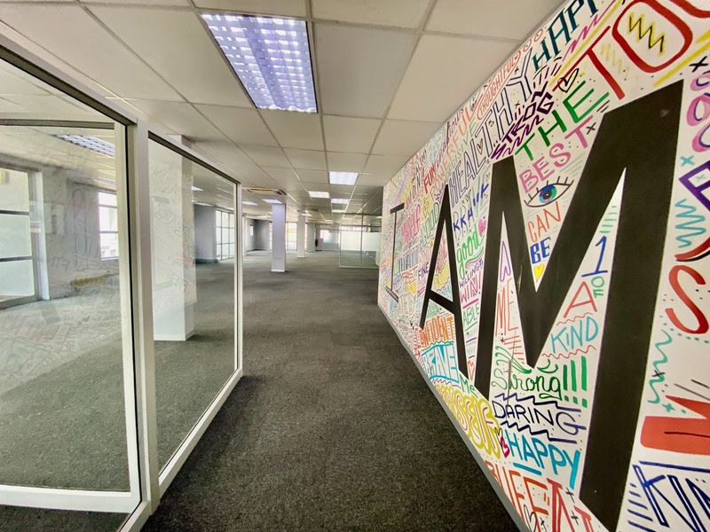 Open-plan commercial office space featuring glass partitions, carpeted flooring, and a suspended ceiling with integrated lighting.