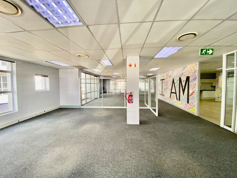 Open-plan commercial office space featuring carpeted flooring, suspended ceilings with recessed lighting, and glass partitioning, providing a versatile and bright work environment.