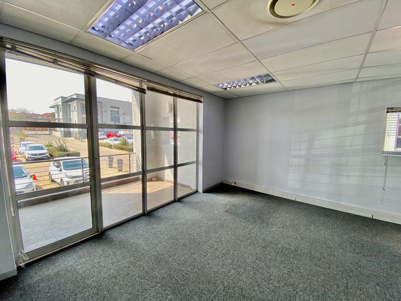 A vacant commercial office space featuring large glass windows, suspended ceilings with recessed lighting, and carpeted flooring, offering a bright and functional workspace.