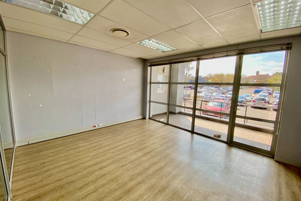 A vacant commercial office space featuring laminate flooring, a suspended ceiling with recessed lighting, and large windows providing ample natural light.